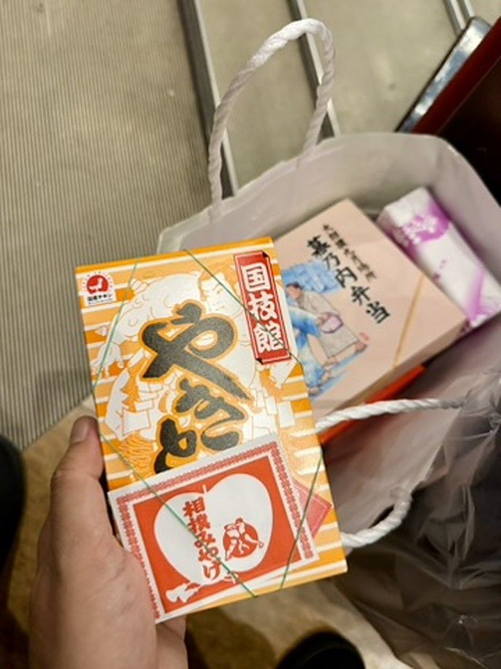 紙袋の前で手に持った、「国技館やきとり」のオレンジ色の箱